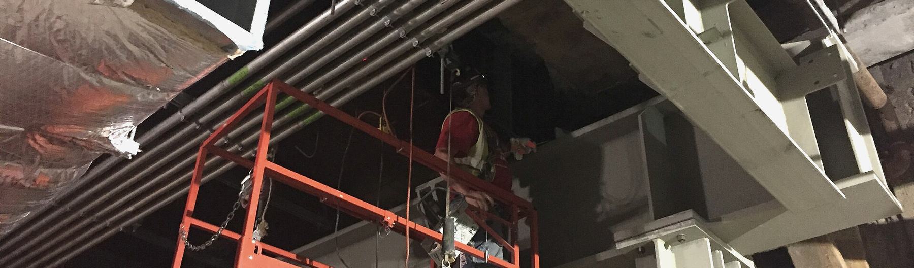 Ironworkers on a lift preparing steel beams overhead